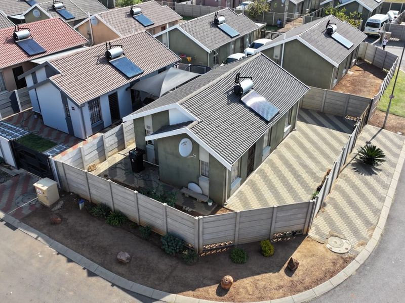Aerial view of a residential property featuring a tiled roof with a solar water heater, paved driveway, and secure precast concrete boundary walls.