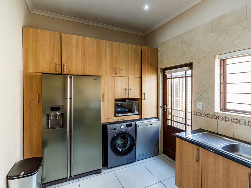 A functional scullery featuring wood-finish cabinetry, tiled backsplash, stainless steel sink, and direct access to the exterior via a secure door.