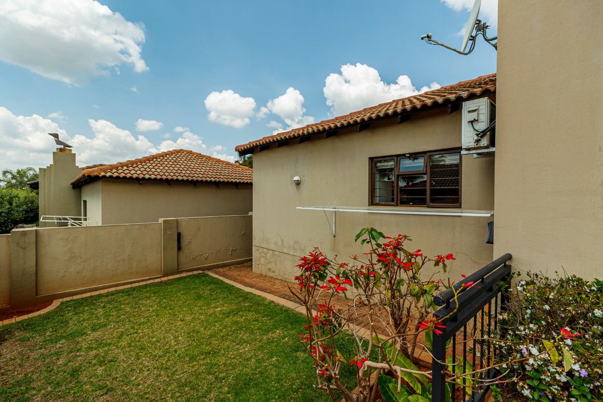 Rear exterior view of the townhouse featuring a small lawn, brick paved pathway, and wall-mounted infrastructure including an air conditioning unit and clothesline.