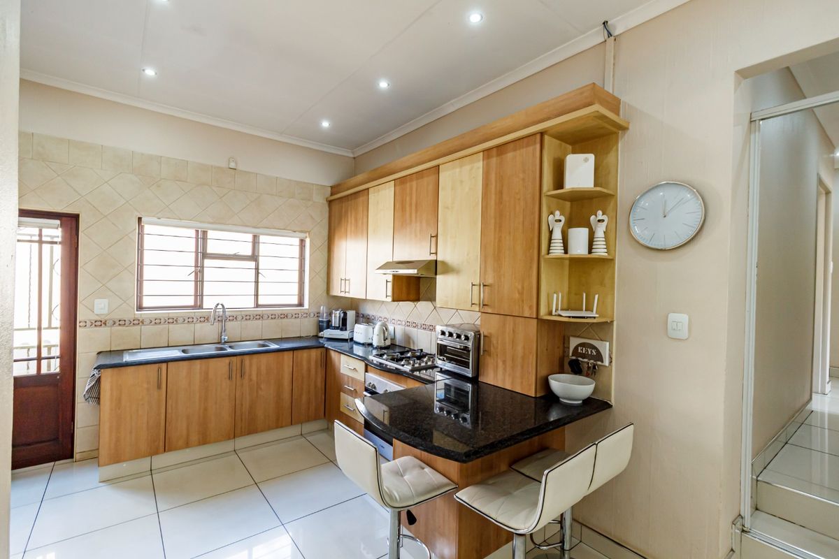 A functional kitchen featuring light wood cabinetry, granite countertops, a gas hob with extractor, and a convenient breakfast bar area with tiled flooring.