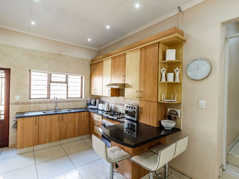 A functional kitchen featuring light wood cabinetry, granite countertops, a gas hob with extractor, and a convenient breakfast bar area with tiled flooring.