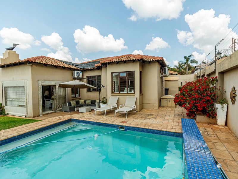 Rear exterior view featuring a swimming pool, paved patio area, and established garden boundary with perimeter security fencing.
