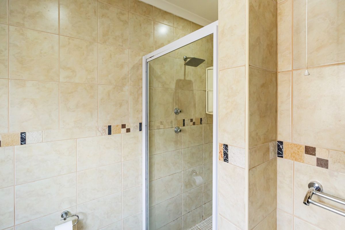 A functional bathroom featuring a glass-enclosed shower with tiled walls and chrome fixtures, presenting a clean and well-maintained space.