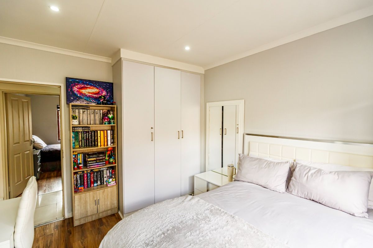 A well-maintained bedroom featuring built-in wardrobes, recessed downlighting, and laminate flooring, with a neutral color palette and clean finishes.
