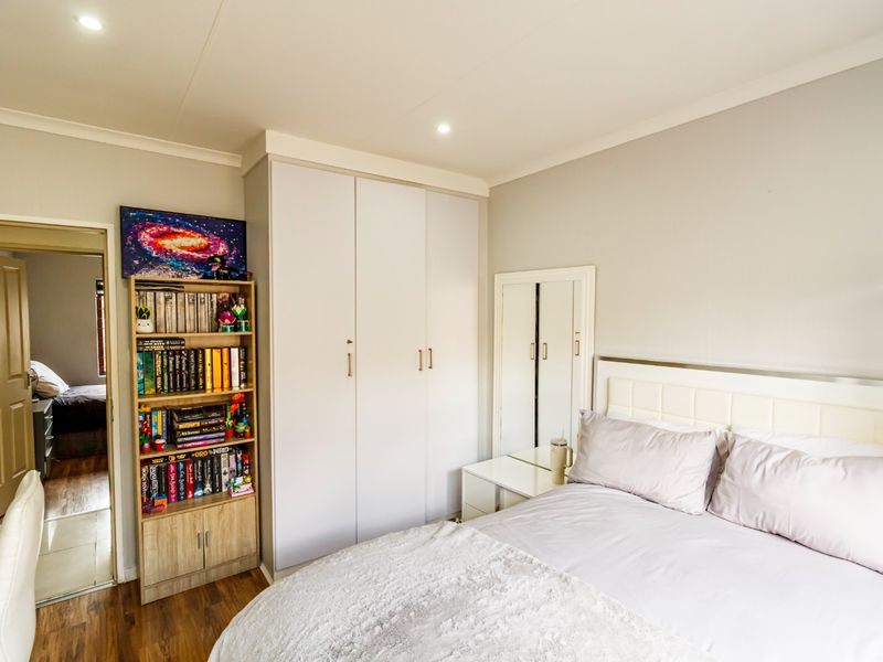 A well-maintained bedroom featuring built-in wardrobes, recessed downlighting, and laminate flooring, with a neutral color palette and clean finishes.