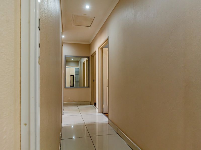 A clean and functional hallway featuring neutral wall tones, tiled flooring, and recessed downlighting, providing access to adjacent rooms.