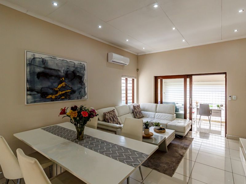 A bright open-plan living and dining area featuring tiled floors, recessed lighting, a wall-mounted air conditioner, and sliding doors leading to an enclosed patio.