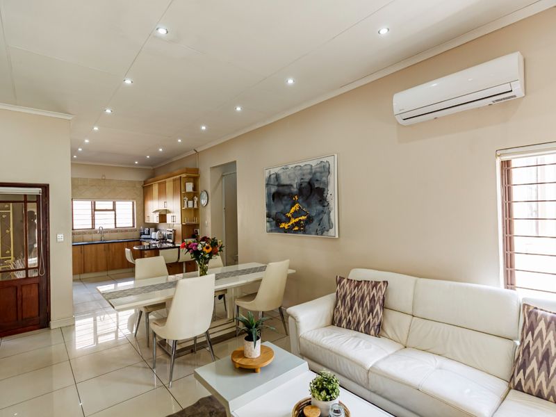Open-plan living and dining area featuring tiled floors, recessed lighting, and a split-system air conditioner, flowing into a functional kitchen space.