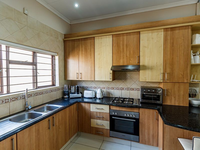 A functional kitchen featuring wood-tone cabinetry, granite countertops, a gas hob, built-in oven, and a double stainless steel sink with tiled backsplash.