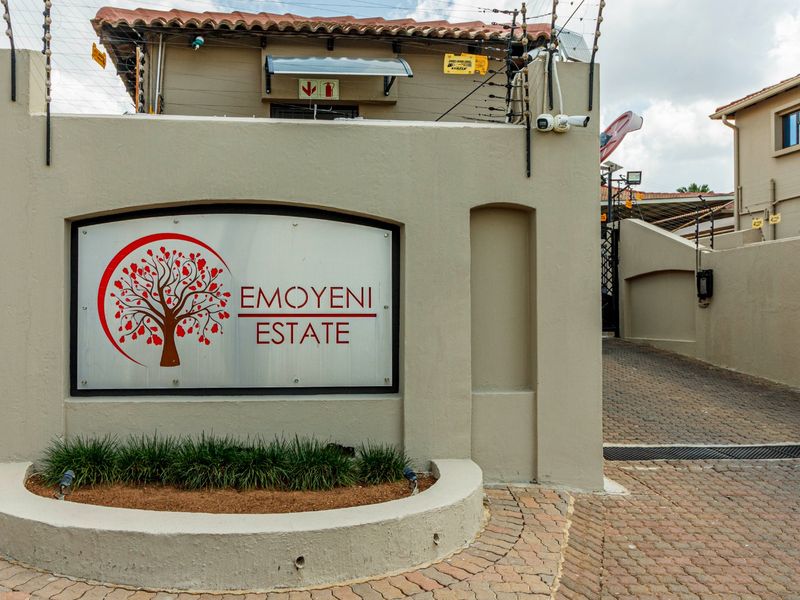 The entrance to Emoyeni Estate featuring a paved driveway, perimeter wall with electric fencing, and security surveillance infrastructure.