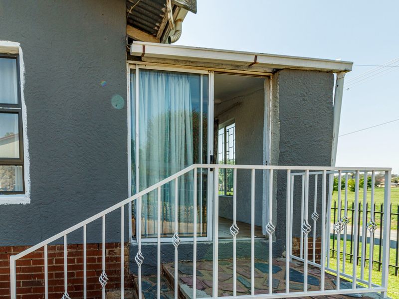 An exterior view of a small patio area featuring stone paving, a white metal railing, and a sliding glass door entrance.