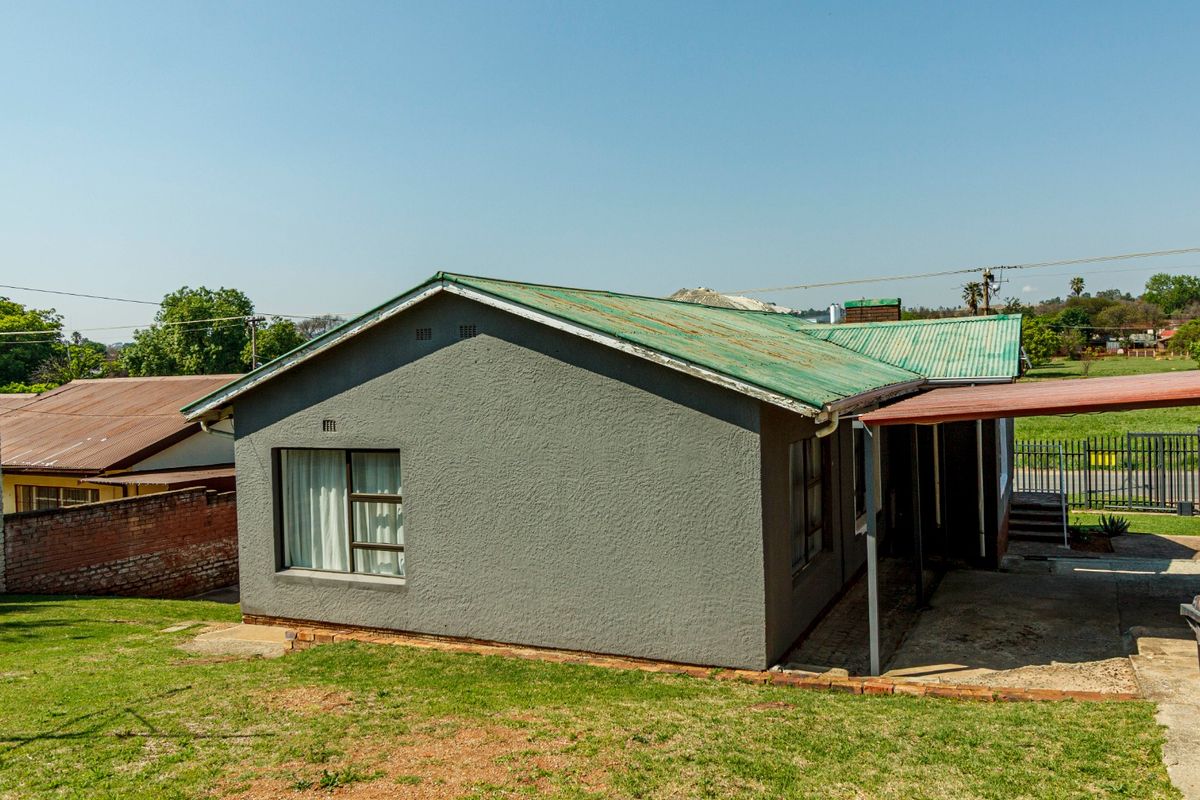 Rear view of a detached house featuring a corrugated metal roof, textured exterior walls, and a covered patio area overlooking the garden.