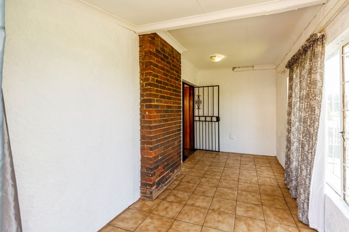 An empty living area featuring an exposed brick pillar, ceramic tiled flooring, and a security gate entrance.