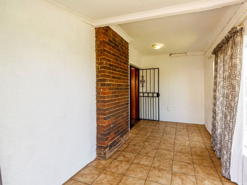 An empty living area featuring an exposed brick pillar, ceramic tiled flooring, and a security gate entrance.