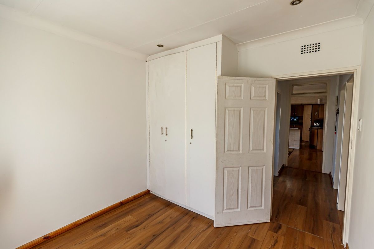 An empty bedroom featuring laminate flooring, built-in cupboards, and recessed ceiling lighting, with a view into the adjacent hallway.