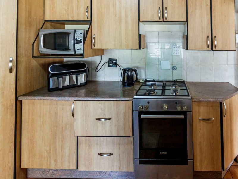 A functional kitchen featuring light wood-finish cabinetry, laminate countertops, a tiled backsplash, and a built-in gas stove with oven.