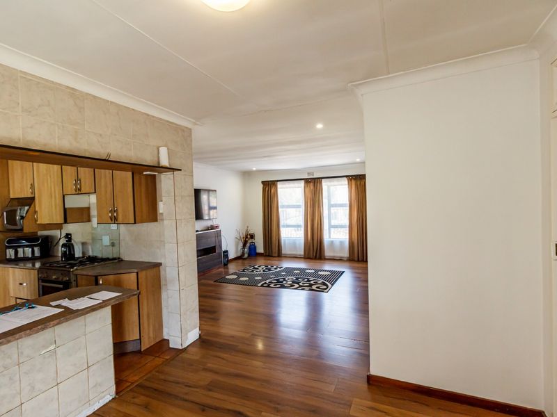 Open-plan living area featuring laminate flooring and a functional kitchen with built-in cabinetry, breakfast bar, and integrated cooking appliances.