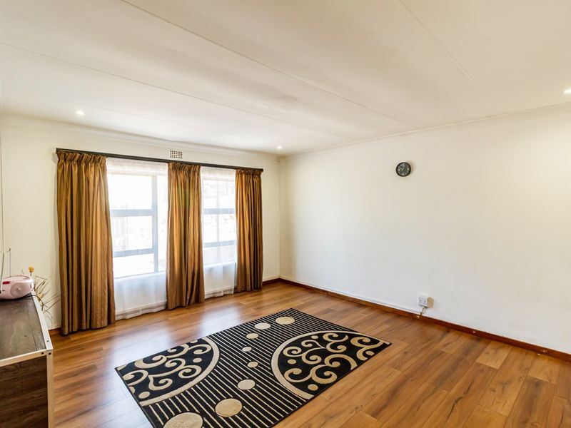 A bright and spacious living room featuring laminate flooring, recessed downlights, and large windows with curtain tracks.