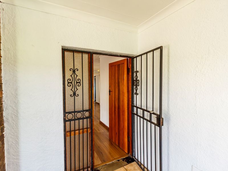 Entrance area featuring a security gate, solid timber door, and textured wall finishes leading into a home with timber flooring.
