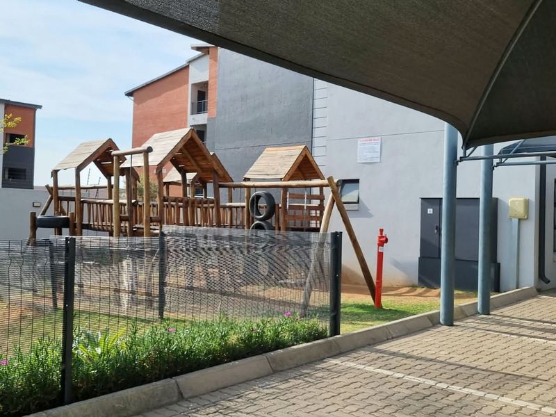 Exterior view of the apartment complex featuring a paved parking area with shade cloth cover and a communal playground facility.