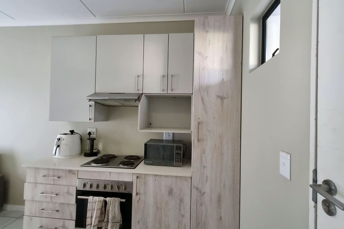 Compact kitchen featuring light wood-grain cabinetry, built-in oven, electric hob, extractor fan, and a tall pantry unit for efficient storage.