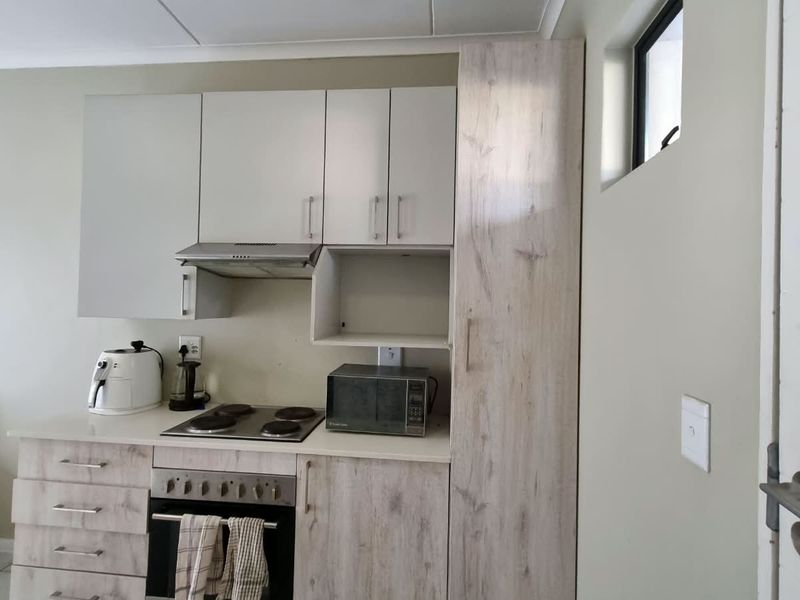 Compact kitchen featuring light wood-grain cabinetry, built-in oven, electric hob, extractor fan, and a tall pantry unit for efficient storage.