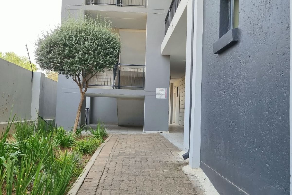 A view of the apartment complex exterior featuring a paved walkway, landscaped garden area, and metal stairwell balustrades.