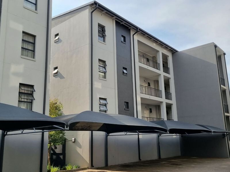 Exterior view of a modern multi-story apartment complex featuring covered parking bays and private balconies.