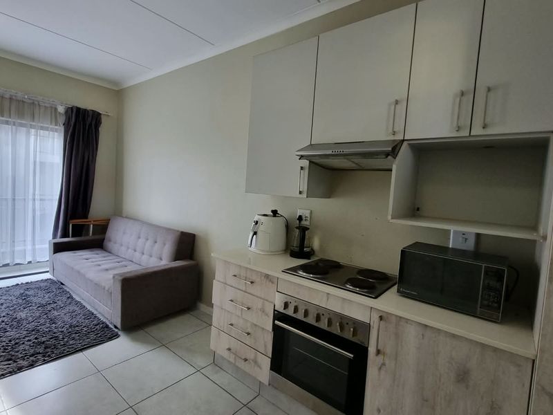 Open-plan living area featuring a compact kitchen with built-in cabinetry, electric hob, oven, and direct access to a balcony through sliding glass doors.