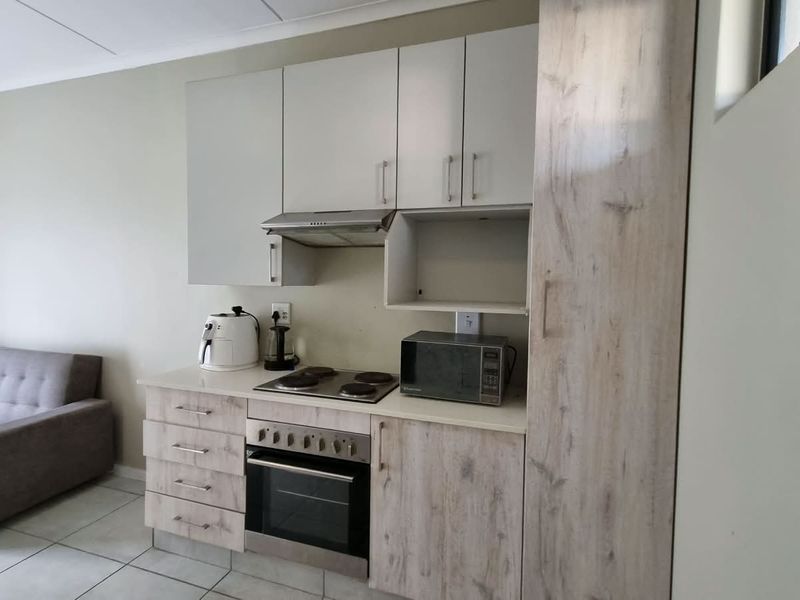Open plan living area featuring a compact kitchen with built-in cabinetry, electric hob, oven, and extractor fan, finished with tiled flooring.