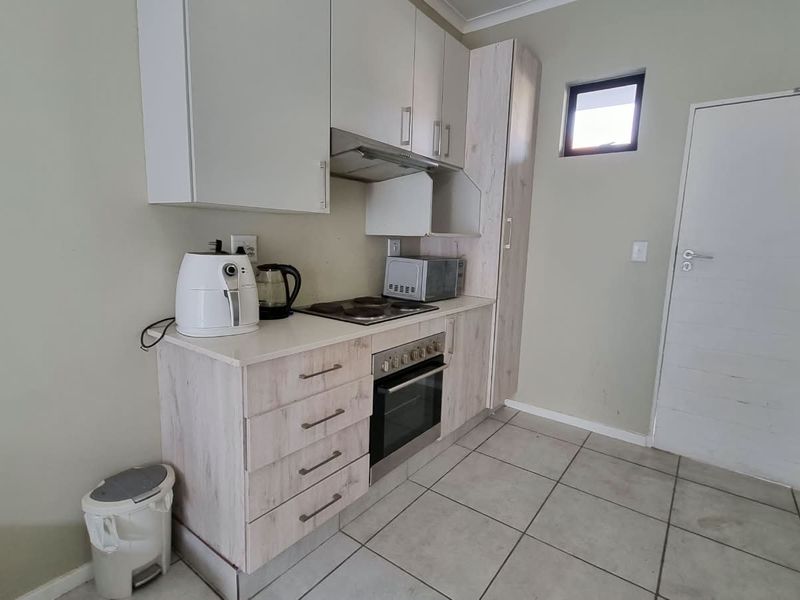 Compact kitchen featuring light wood-look cabinetry, built-in oven, electric hob, extractor fan, and tiled flooring.