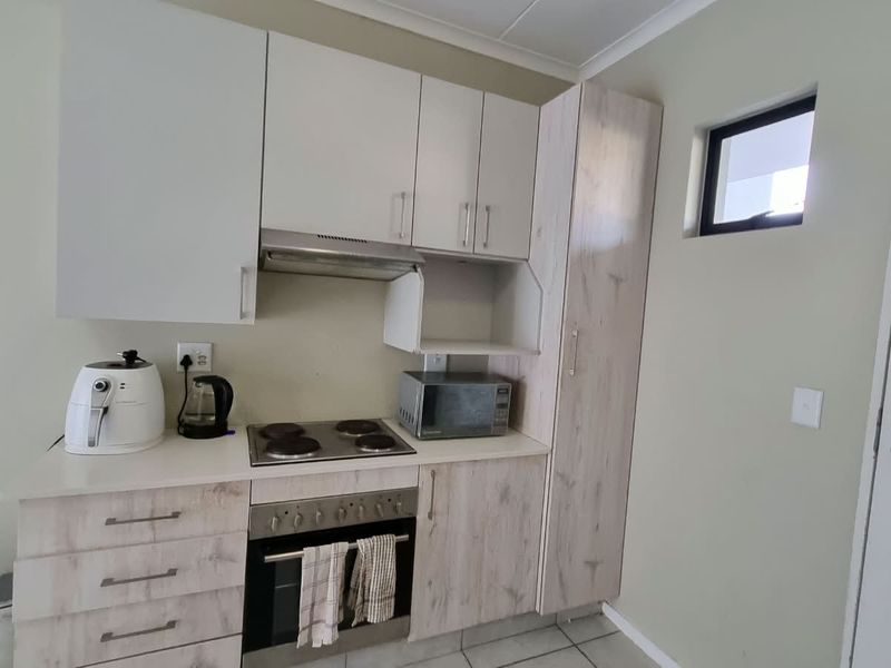Compact kitchen featuring modern light wood-grain cabinetry, built-in electric oven and hob, extractor fan, and tiled flooring.