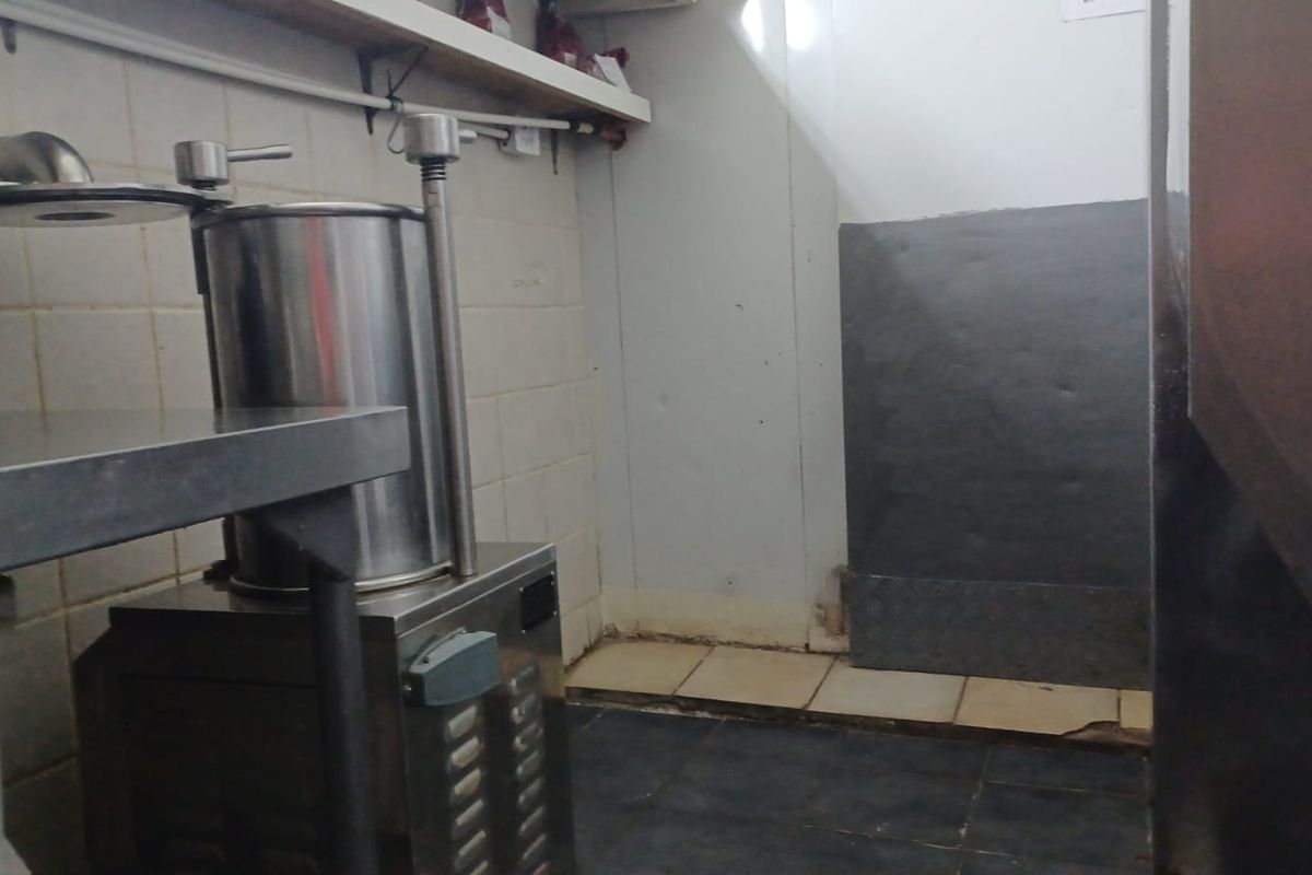 A utilitarian scullery or prep area featuring tiled surfaces and wall-mounted shelving, currently showing signs of wear and requiring maintenance.