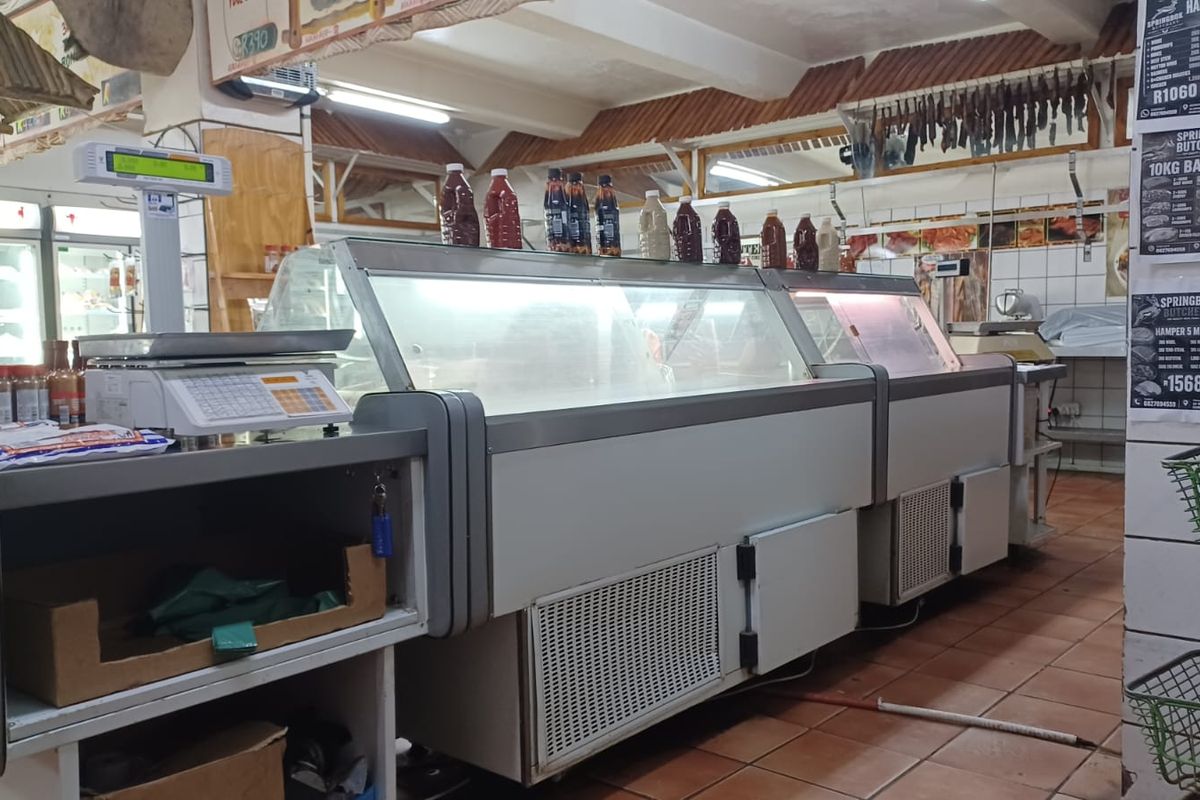 A commercial butchery interior featuring refrigerated display counters, tiled flooring, and exposed ceiling beams.