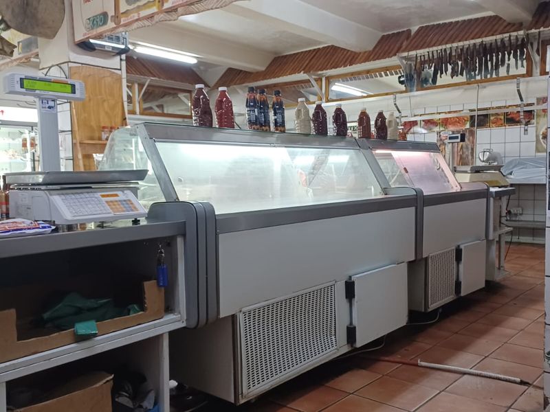A commercial butchery interior featuring refrigerated display counters, tiled flooring, and exposed ceiling beams.