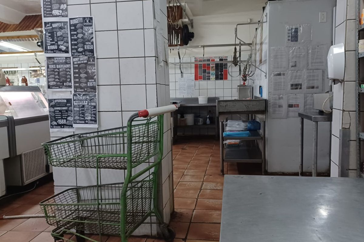 A commercial butchery or utility prep area featuring tiled walls, stainless steel work surfaces, and industrial shelving units.