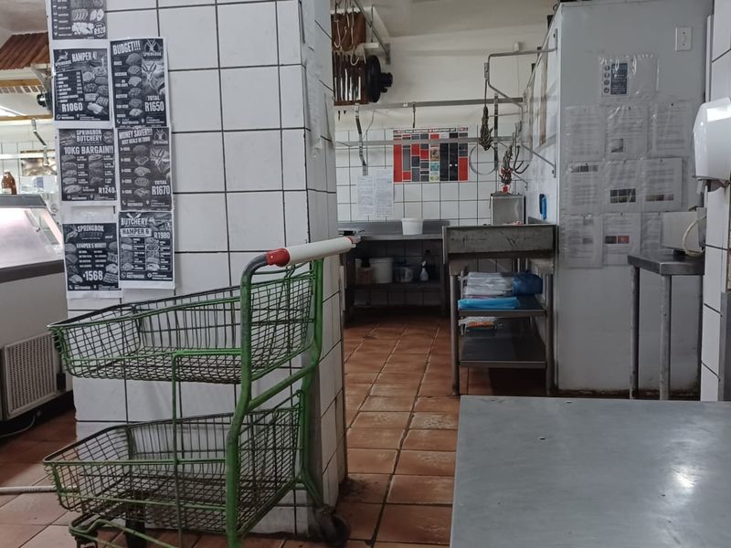 A commercial butchery or utility prep area featuring tiled walls, stainless steel work surfaces, and industrial shelving units.