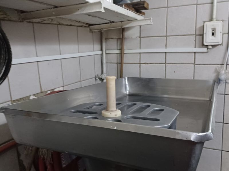 A utilitarian scullery or wash-up area featuring a stainless steel sink, tiled wall finishes, and basic wall-mounted shelving.