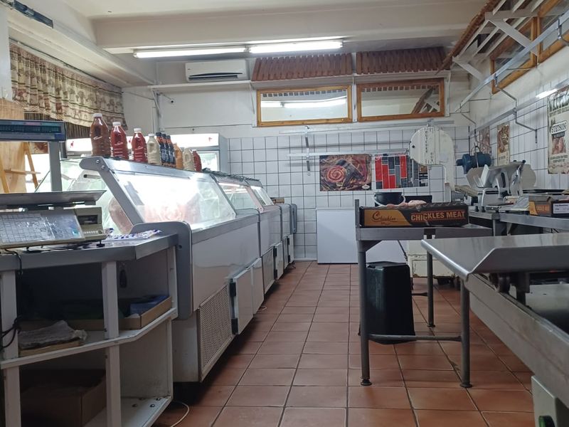 A commercial-style kitchen or butchery area featuring tiled flooring, wall-mounted air conditioning, and multiple refrigeration units.