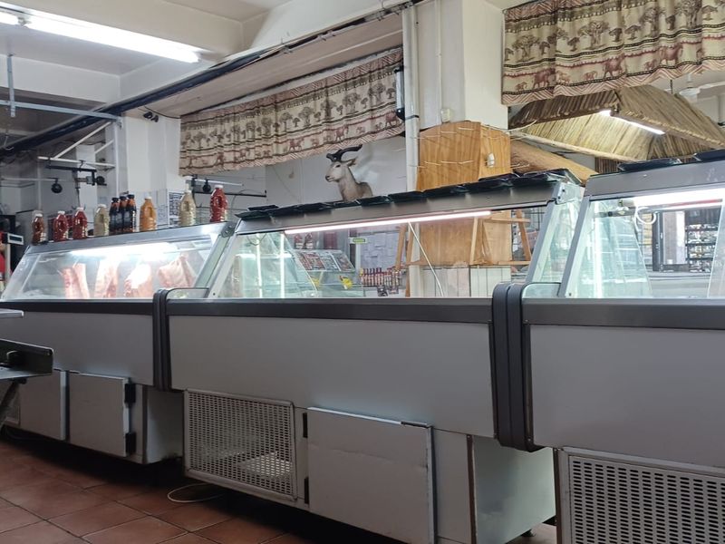 A commercial kitchen space featuring multiple refrigerated display counters and tiled flooring, suitable for food preparation or retail butchery operations.