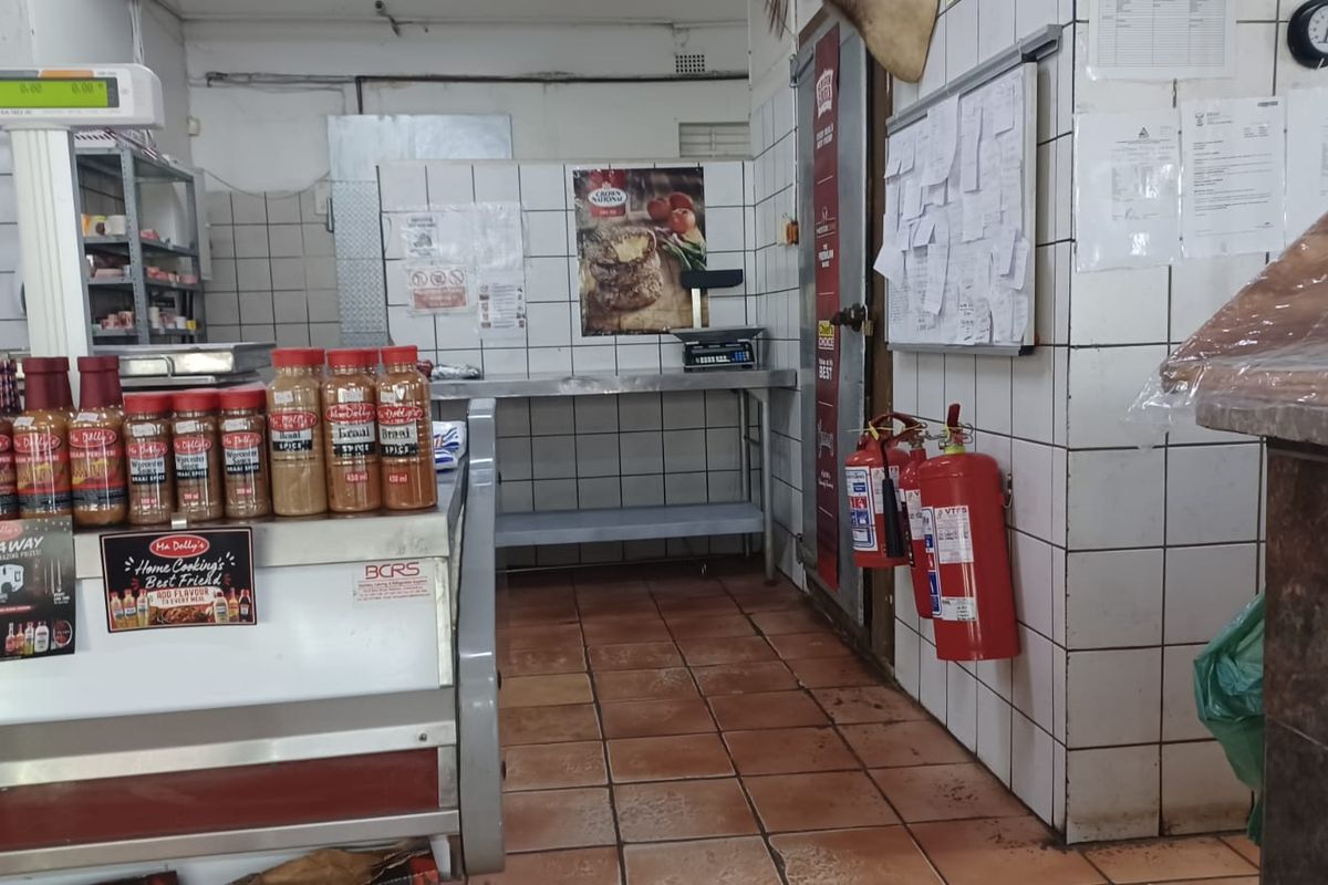 A commercial-style kitchen area featuring tiled walls, durable floor tiles, stainless steel prep surfaces, and wall-mounted fire safety equipment.