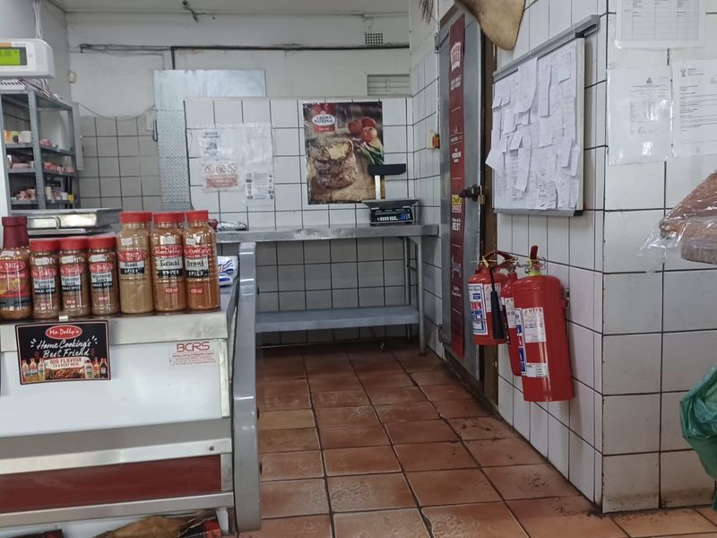 A commercial-style kitchen area featuring tiled walls, durable floor tiles, stainless steel prep surfaces, and wall-mounted fire safety equipment.