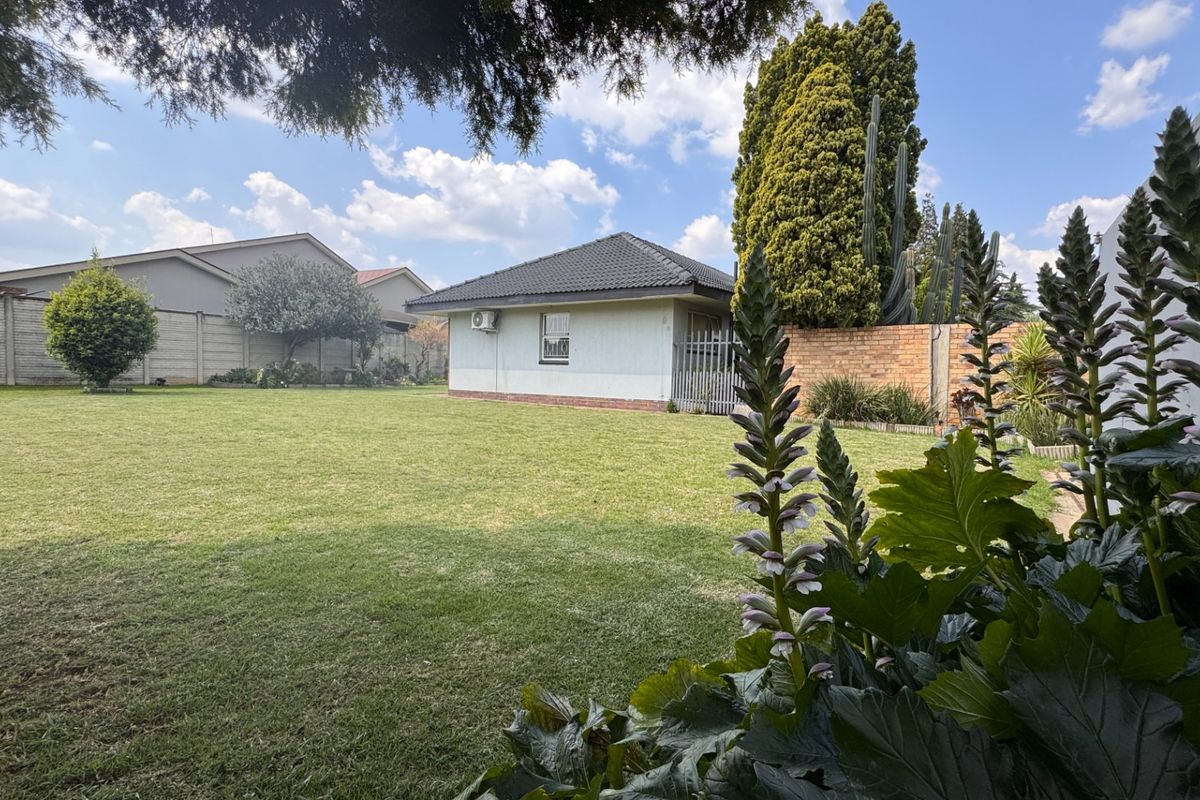 Spacious rear garden featuring a well-maintained lawn, perimeter boundary walls, and a view of the rear building elevation with an installed air conditioning unit.