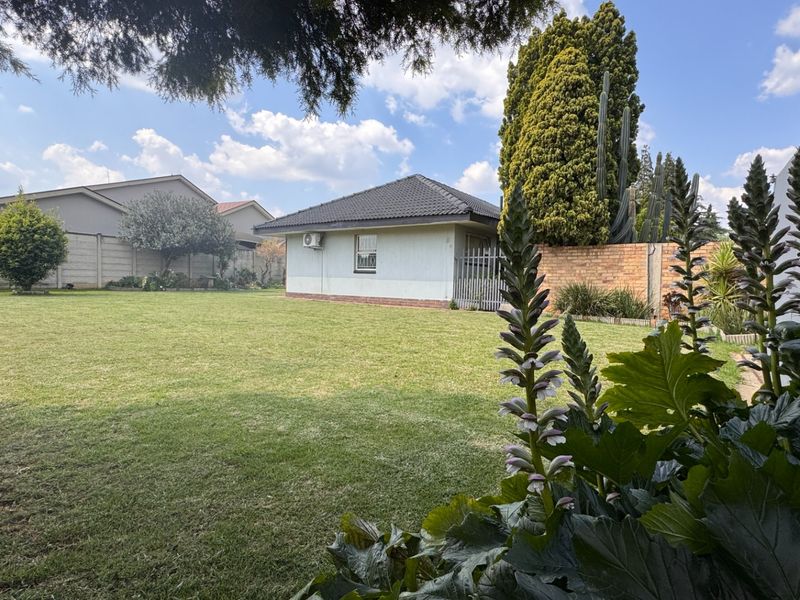 Spacious rear garden featuring a well-maintained lawn, perimeter boundary walls, and a view of the rear building elevation with an installed air conditioning unit.