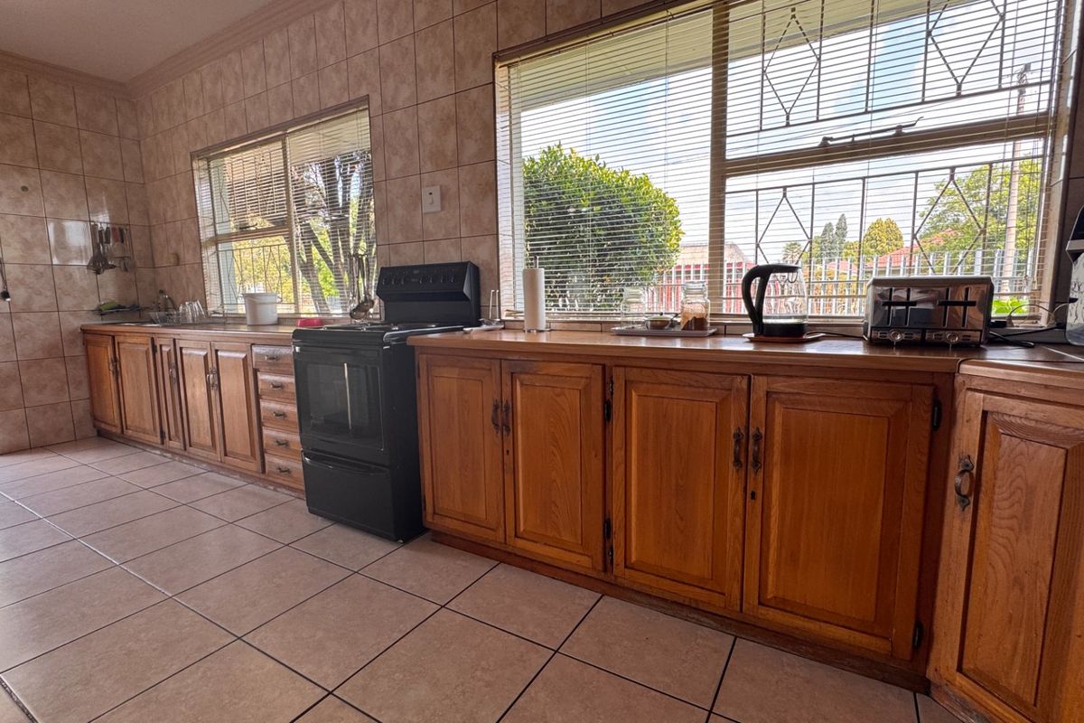 A functional kitchen featuring wooden cabinetry, tiled walls and flooring, and a freestanding stove, with large windows providing natural light.