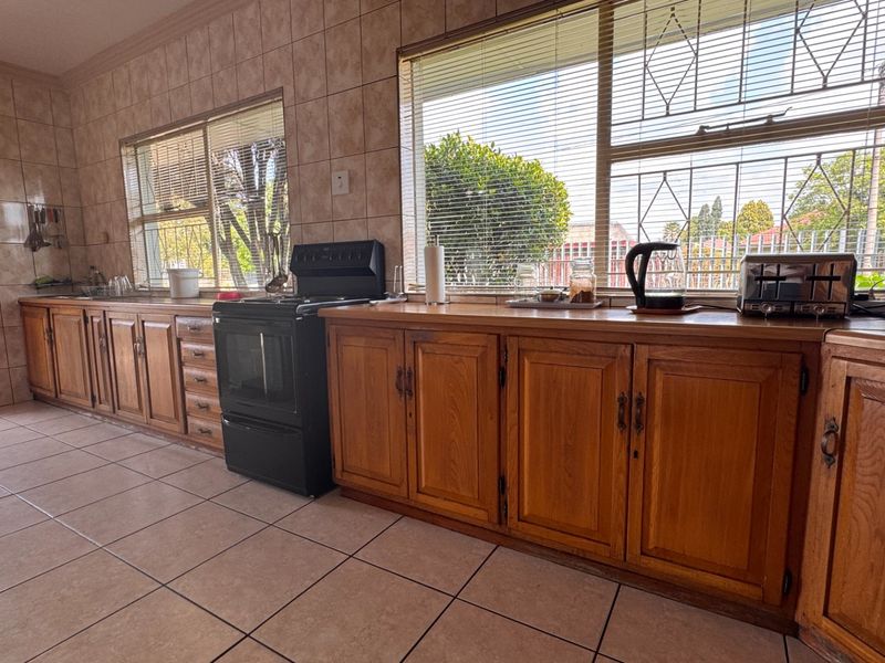 A functional kitchen featuring wooden cabinetry, tiled walls and flooring, and a freestanding stove, with large windows providing natural light.