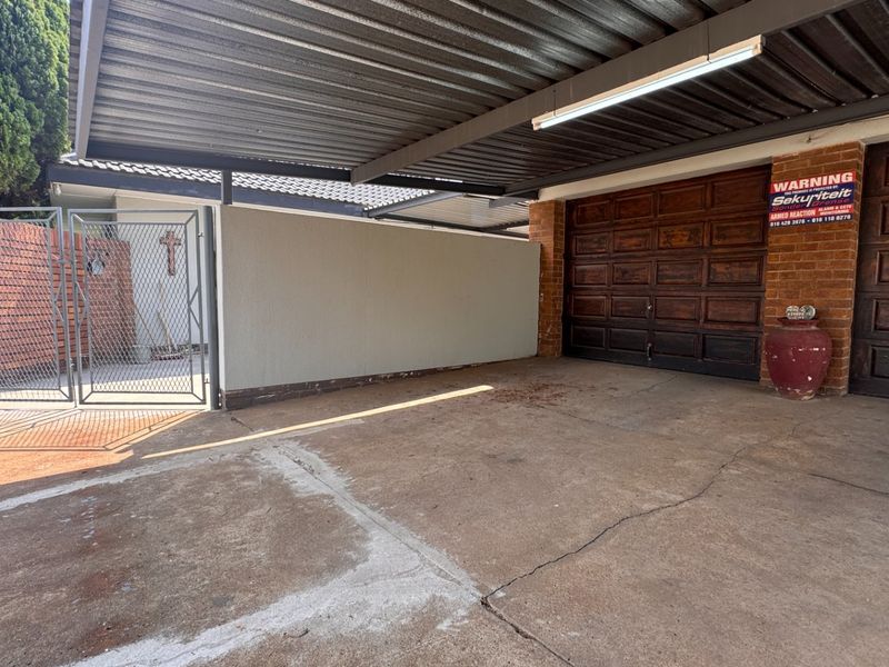 A covered double garage area featuring wooden doors, concrete flooring, and a secure gated entrance with a brick boundary wall.