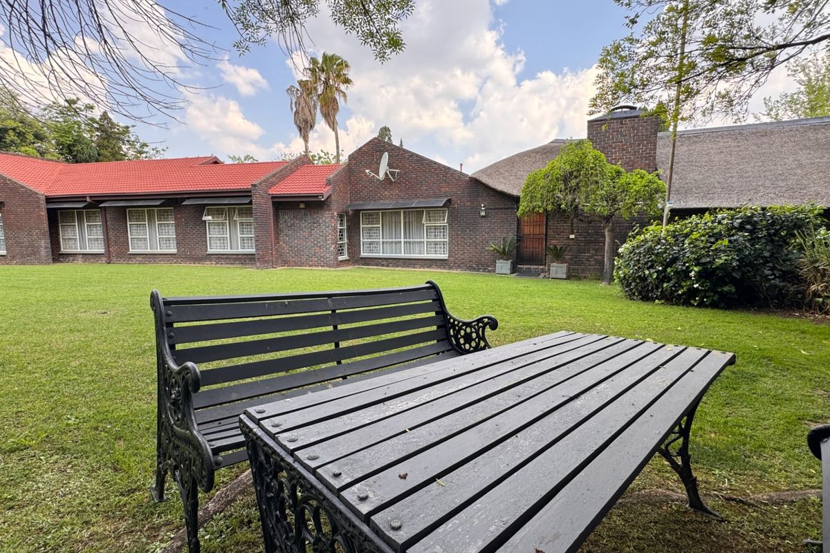A spacious rear garden view featuring a well-maintained lawn, brick exterior walls, and a combination of tiled and thatched roofing.