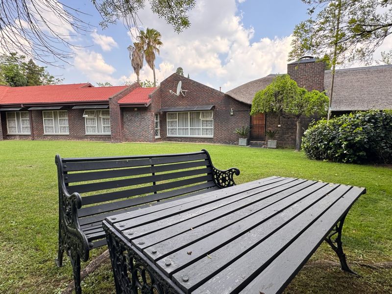 A spacious rear garden view featuring a well-maintained lawn, brick exterior walls, and a combination of tiled and thatched roofing.