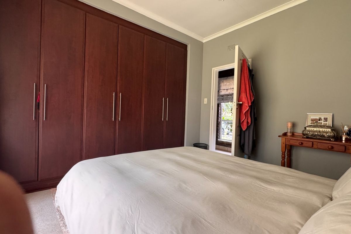 A well-maintained bedroom featuring extensive dark wood built-in cupboards, neutral wall tones, and carpeted flooring.